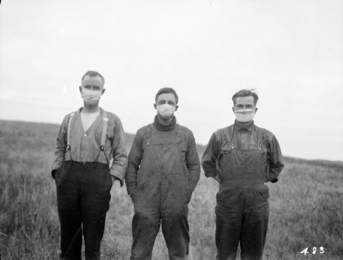 black and white photo of three men wearing masks on an Alberta farm during the 1918 pandemic